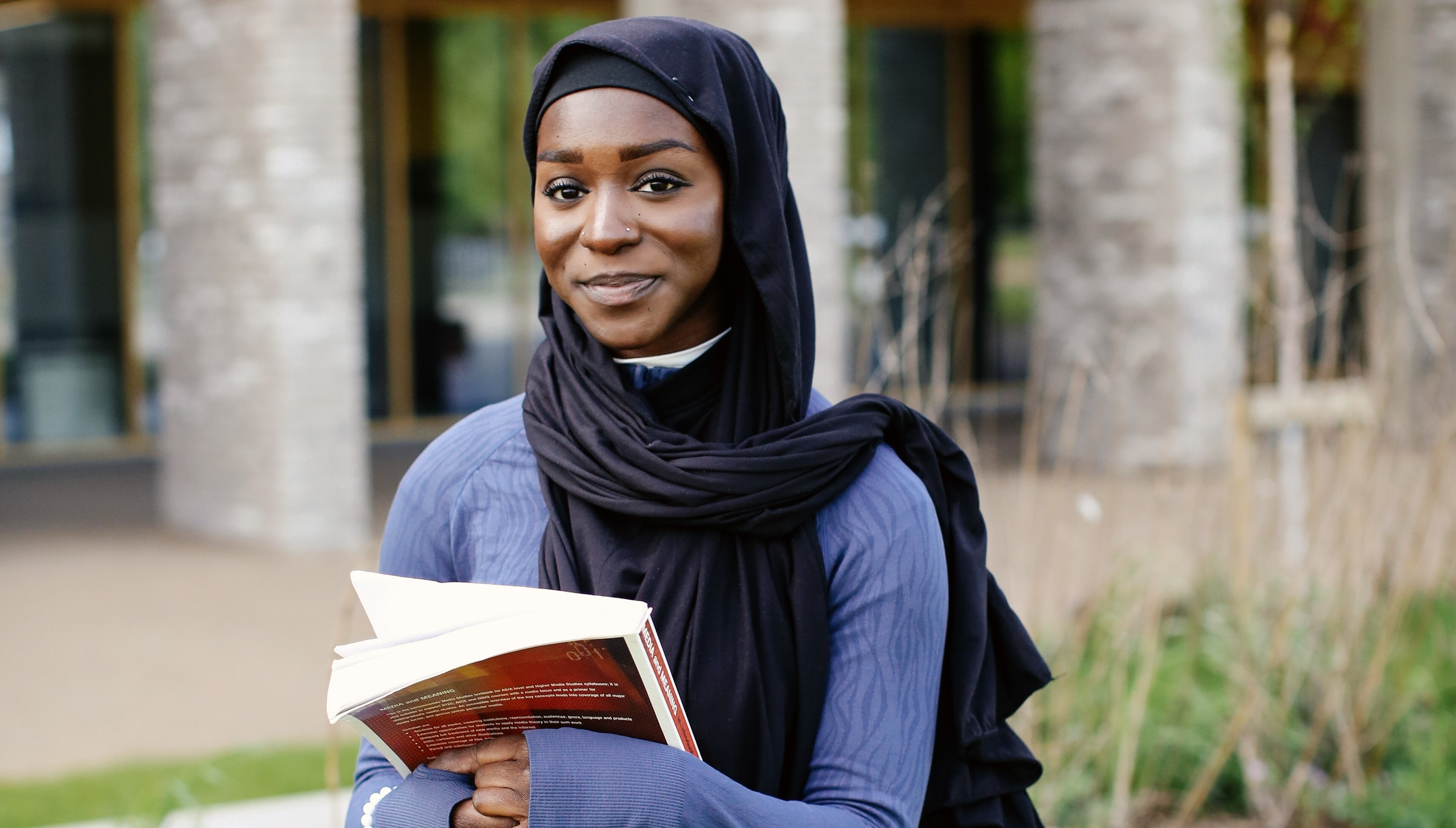 Student standing smiling holding a book