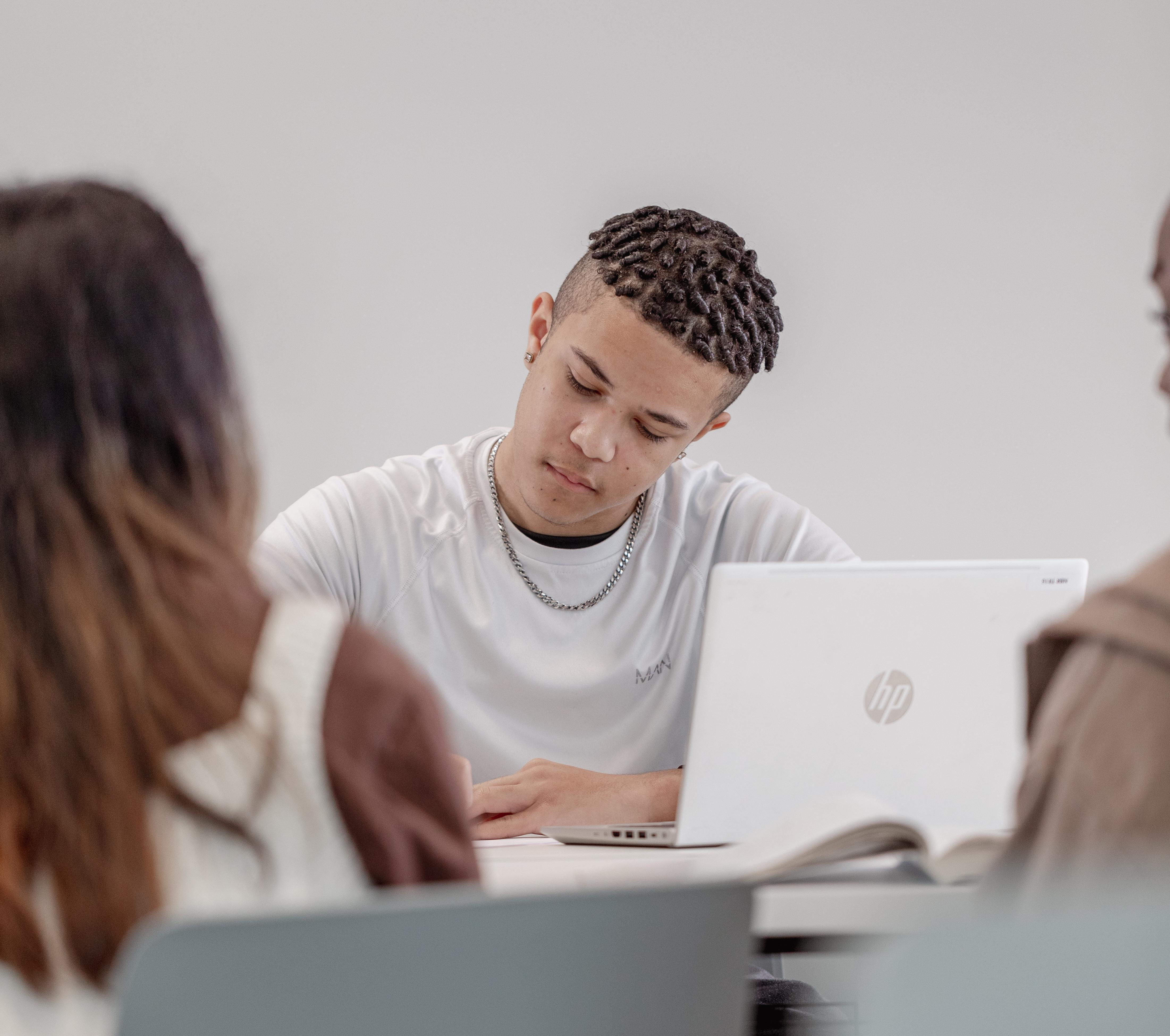Student sat at a desk writing with a laptop open next to him