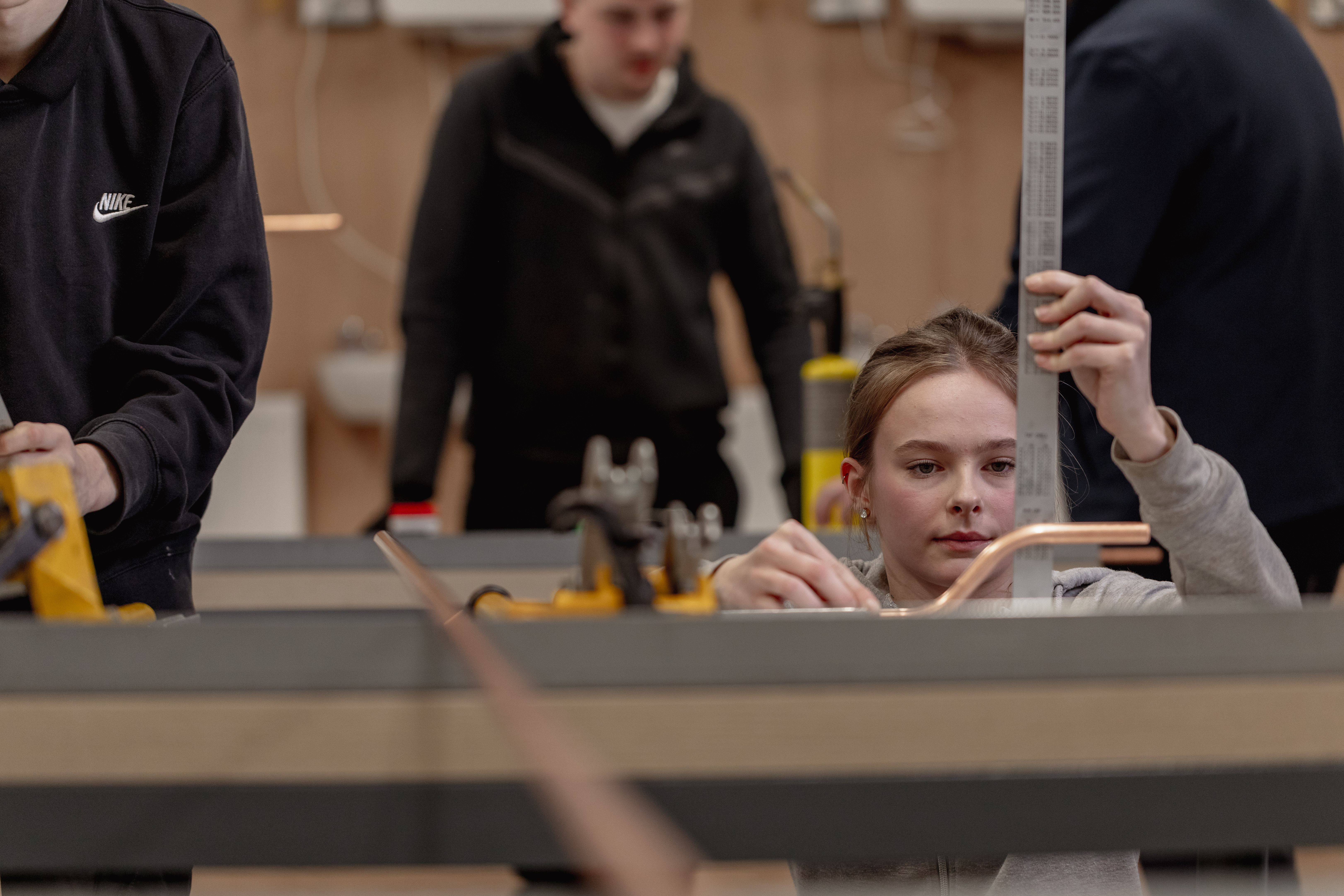 Student in a plumbing workshop measuring a pipe