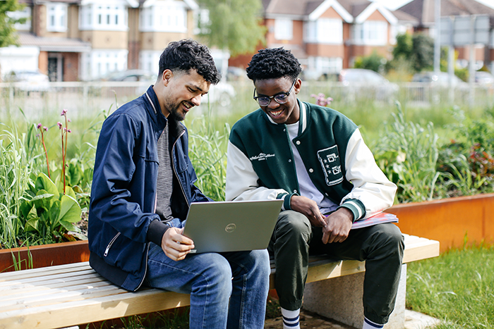 Two boy sitting on a bench both looking at a laptop