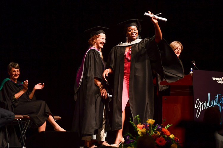 Women on stage in her cap and gown waving her scroll