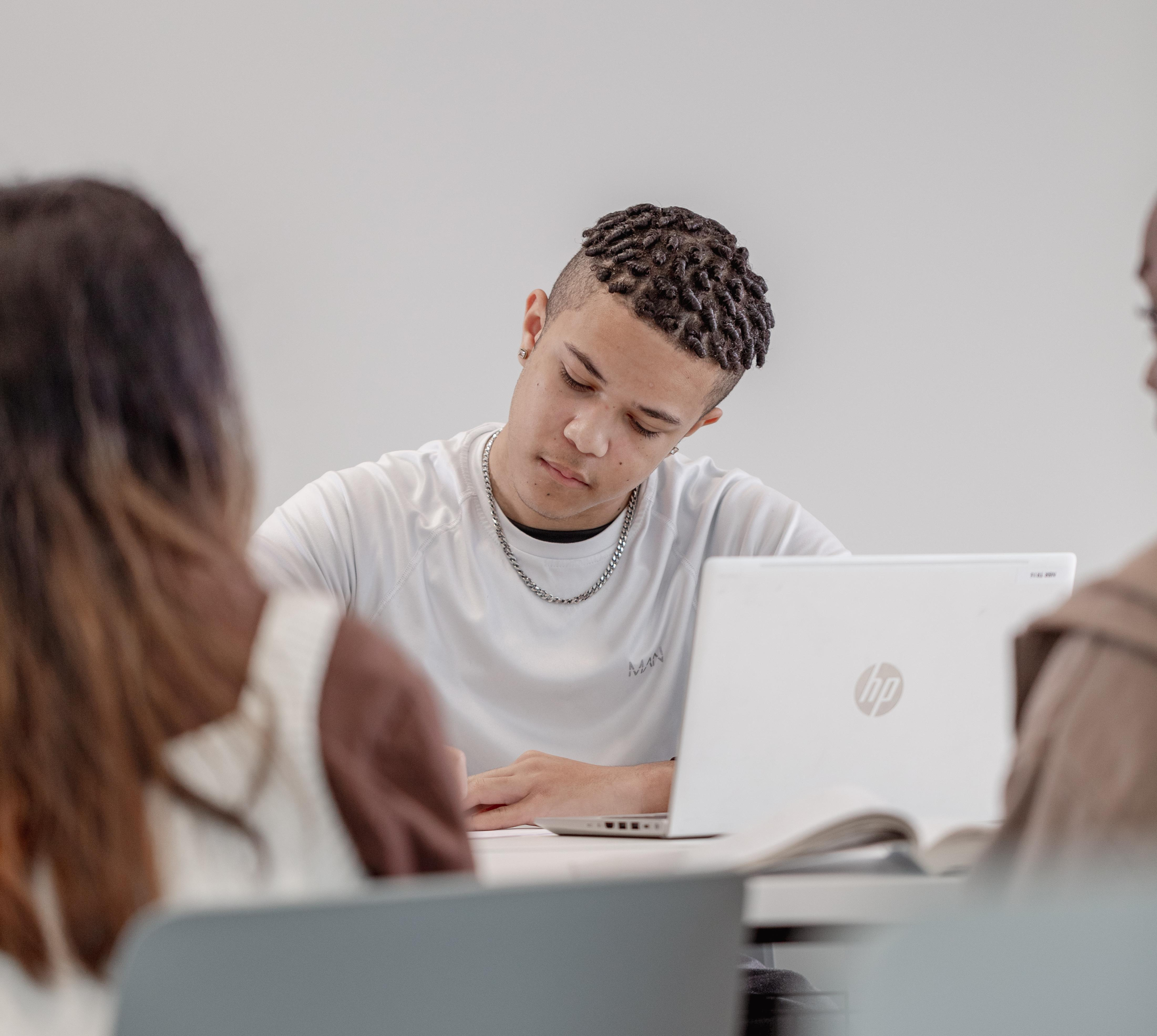 Student sat a desk writing on piece of paper with a laptop on the table
