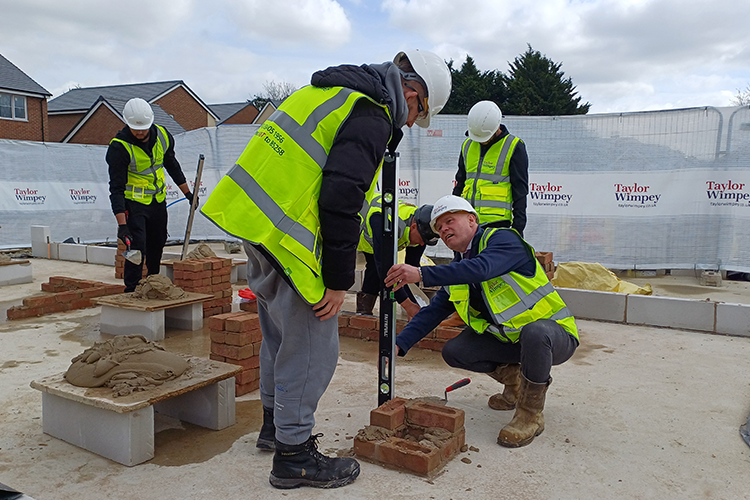 Students being shown bricklaying by Taylor Wimpey employees